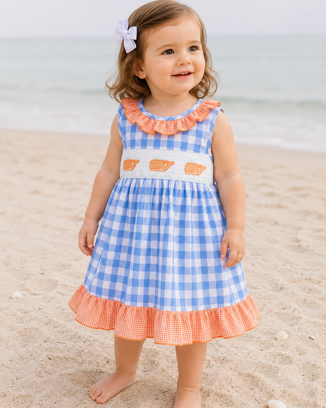 Young girl on beach in plaid dress with whale embroidery.