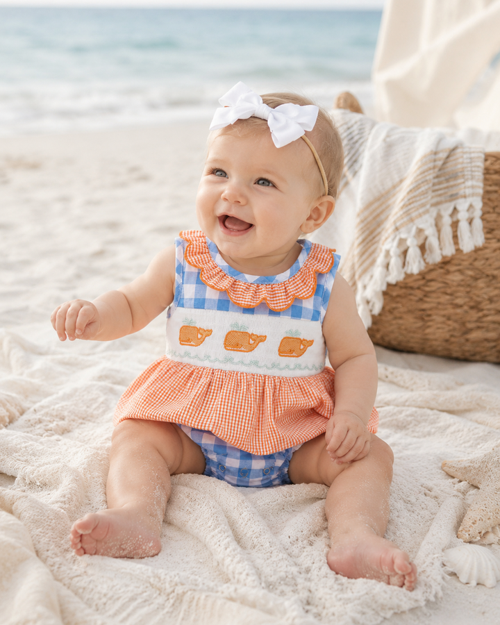 Baby girl on beach in blue and orange plaid romper