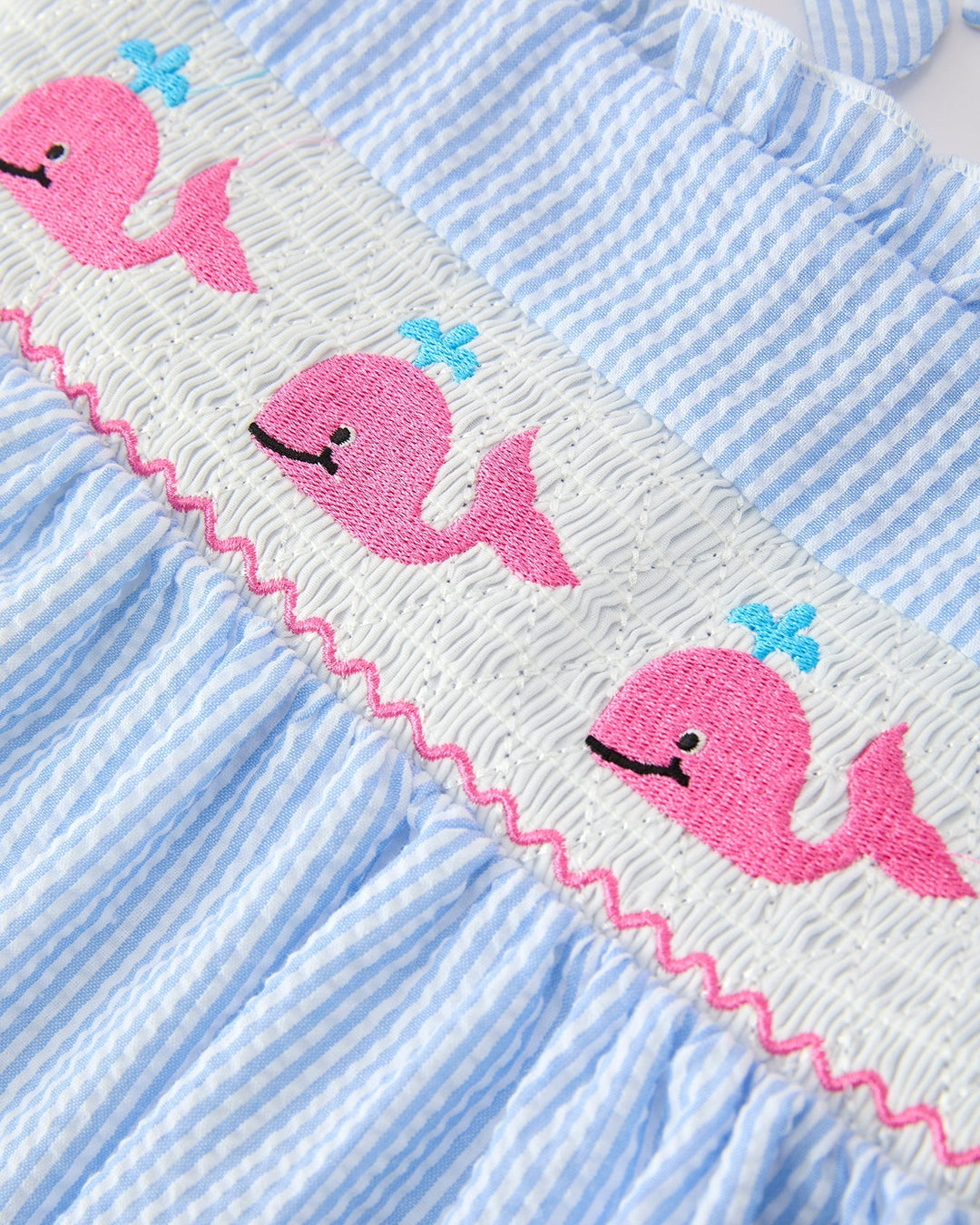 Close-up of a blue and white striped fabric with pink whale designs.