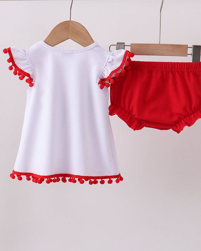 White top with red pom-pom details and red bloomers on hangers against a light gray background