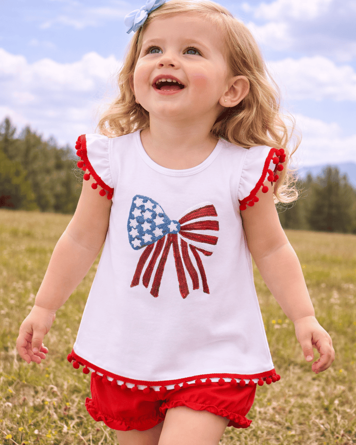 Child wearing a white top with a red, white, and blue flag design and red shorts in a field.