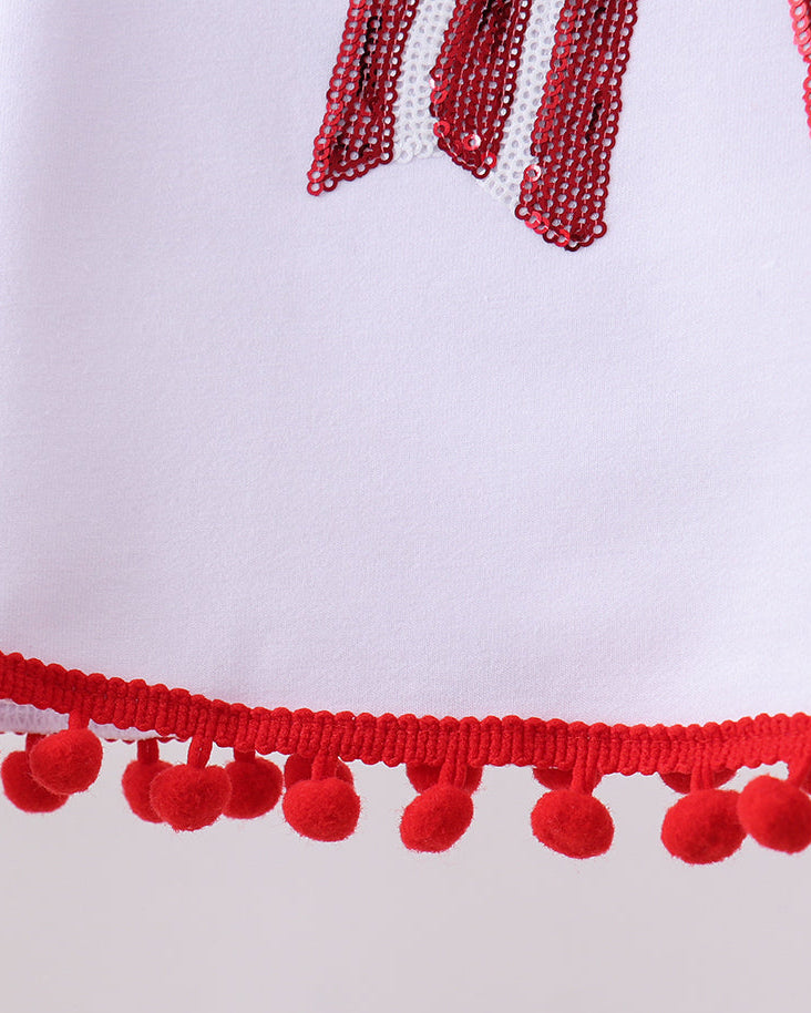 Close-up of a white garment with red tassels and pom-poms on a light gray background