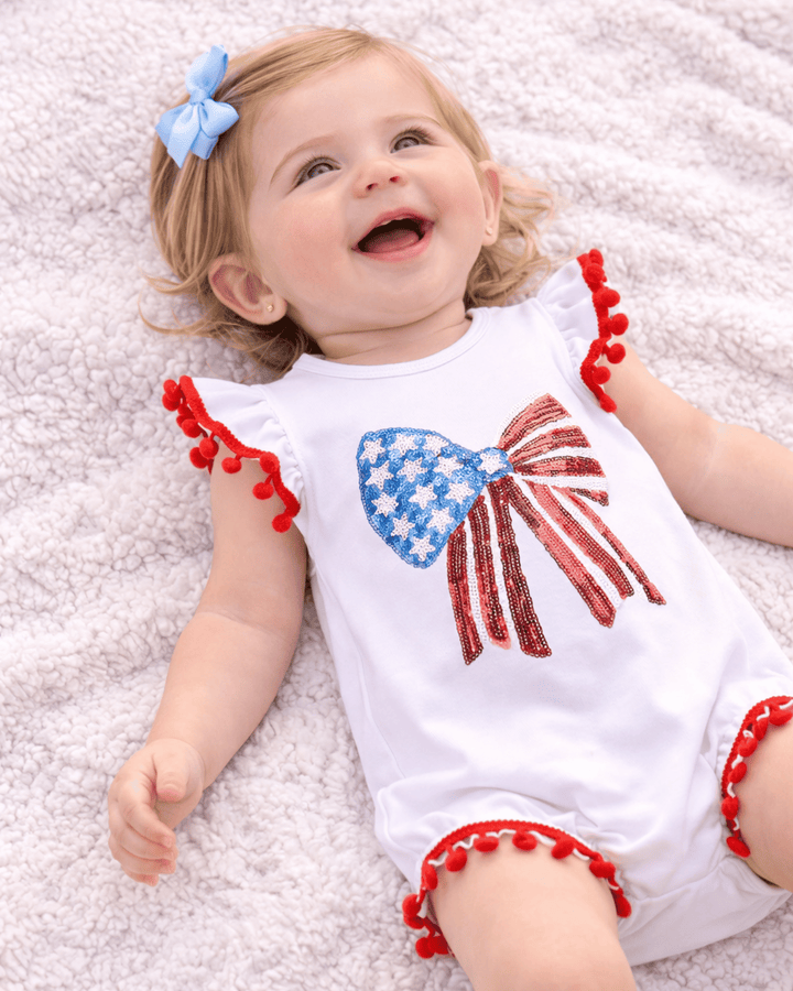 Baby wearing a white romper with red, white, and blue design on a light gray background