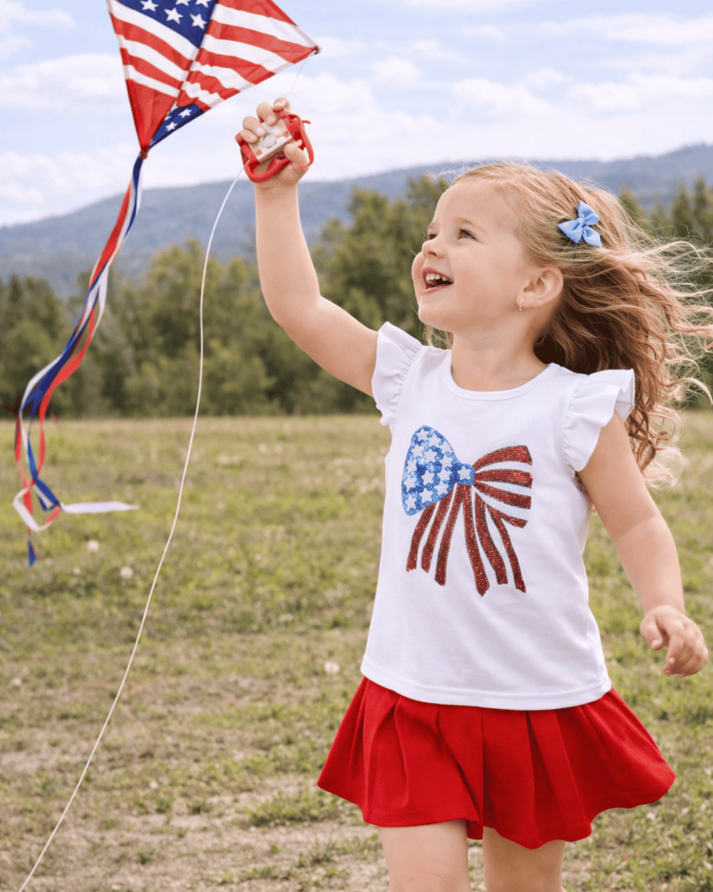 Child holding a kite with an American flag design in a field
