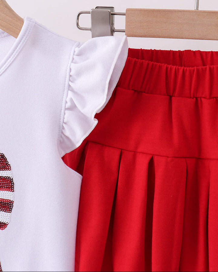 White top with ruffled collar and red pleated skirt on a hanger against a white background