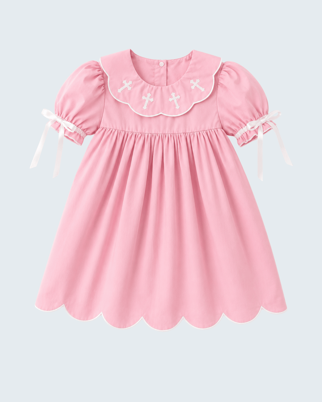 A pink short-sleeve dress with a scalloped Peter Pan collar decorated with white embroidered crosses, featuring puffed sleeves with white ribbon ties, shown against a light gray background.