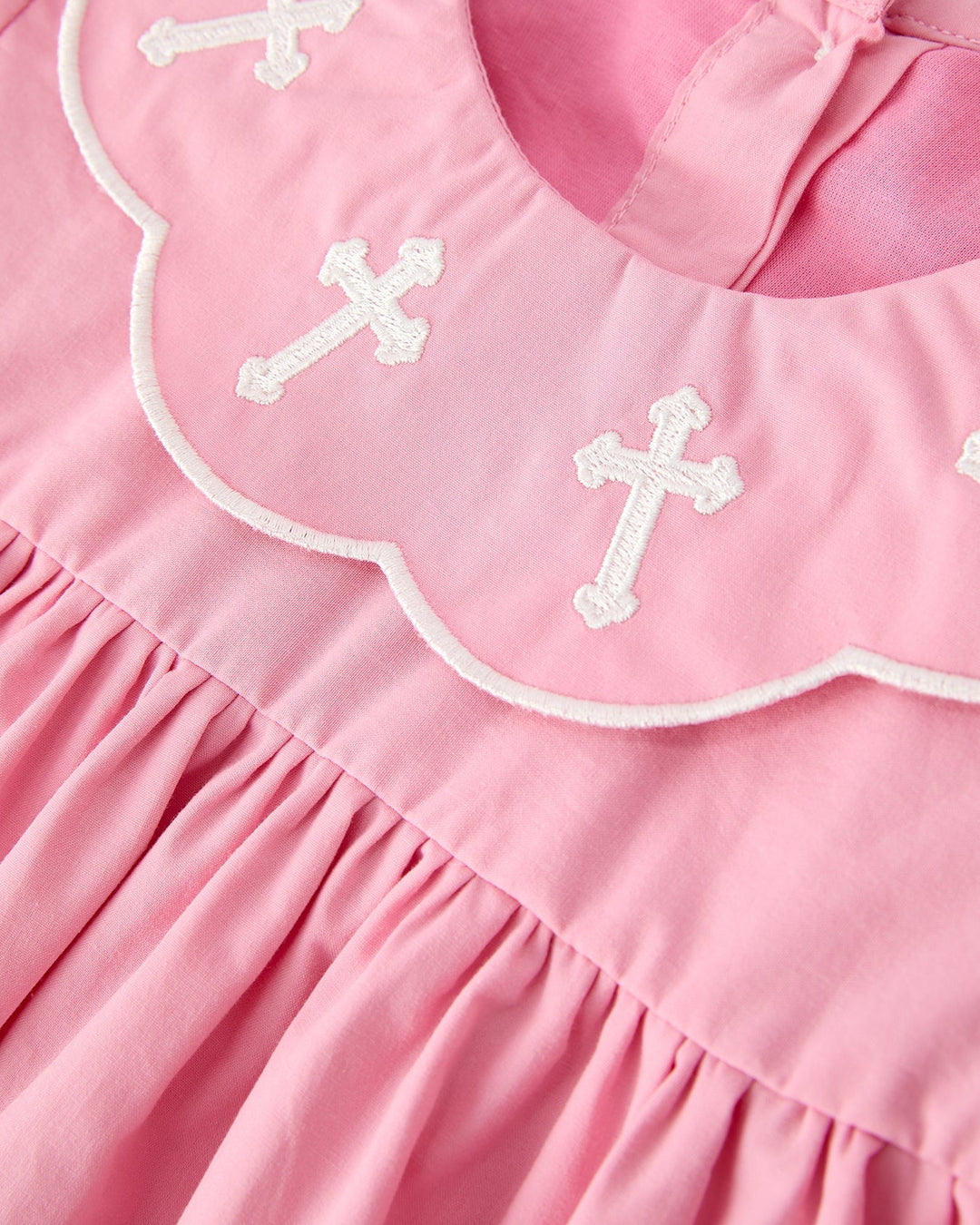 Pink christening dress bib with white embroidered crosses and scalloped white trim