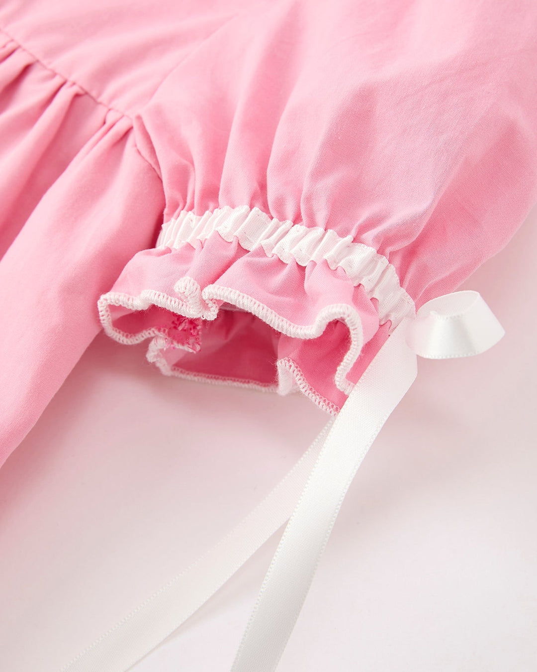 Pink christening dress close-up: white ruffled hem edge and long tie ribbons