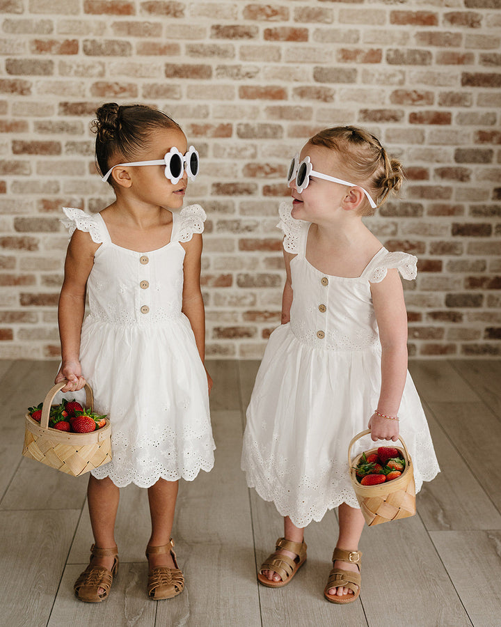 Two young girls in white dresses standing against a brick wall.