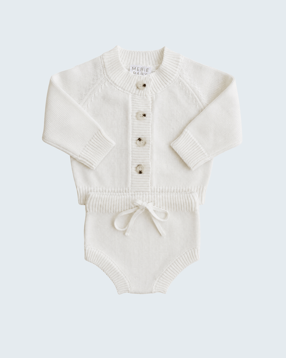 An off-white knit baby romper with long raglan sleeves, a button-up front, and a small drawstring tie at the crotch, shown on a light gray background.