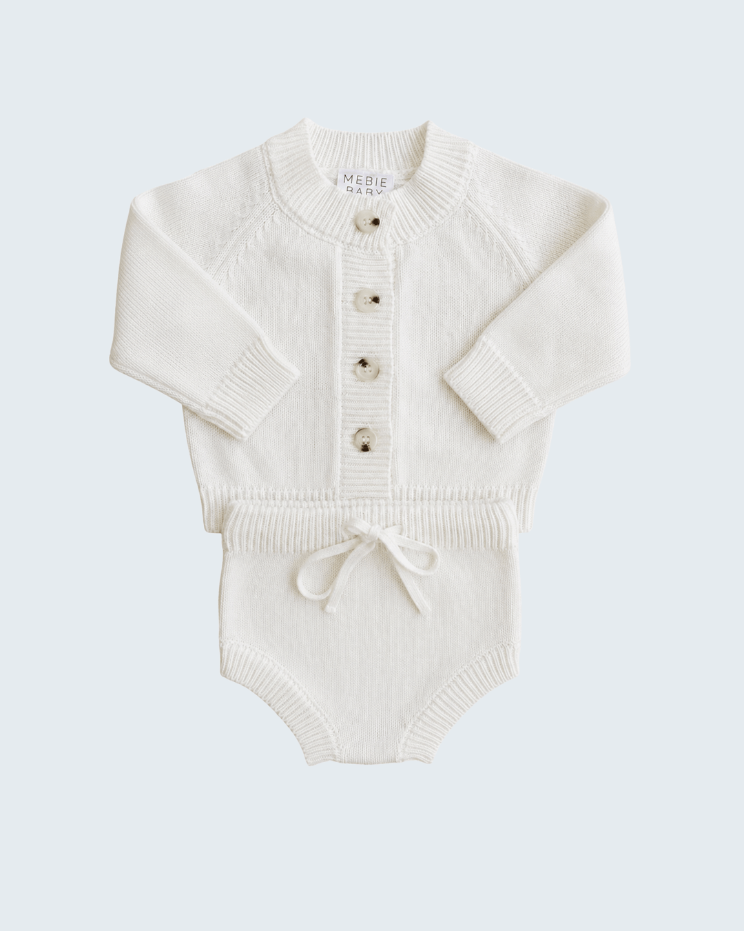 An off-white knit baby romper with long raglan sleeves, a button-up front, and a small drawstring tie at the crotch, shown on a light gray background.