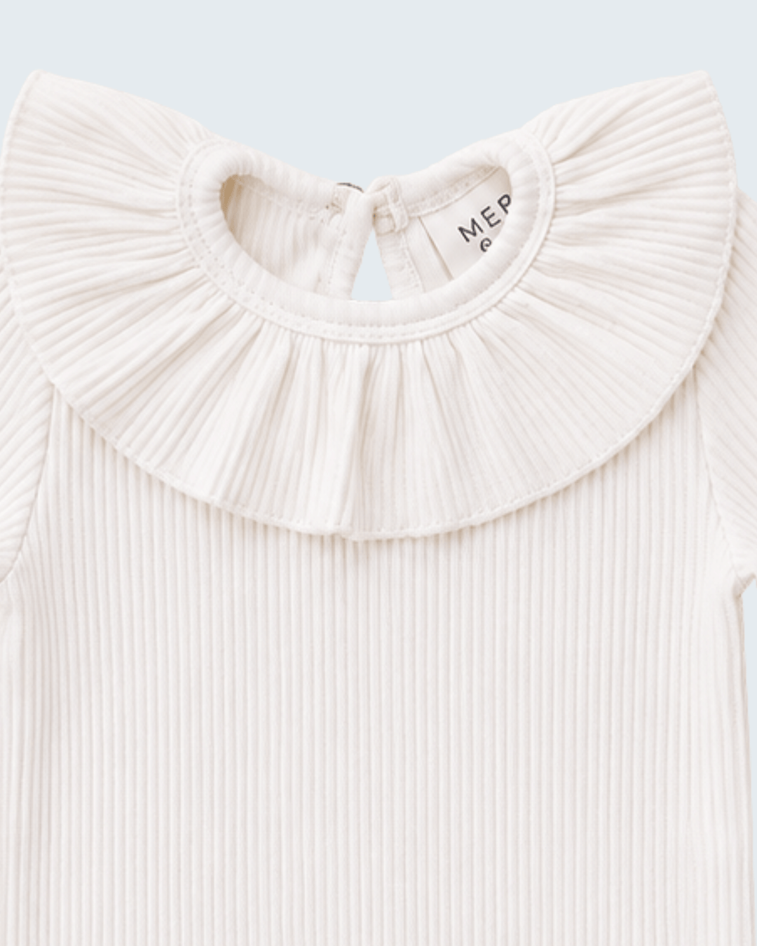 Close-up of a ribbed cream baby top featuring a large pleated ruffled collar, with the brand name &