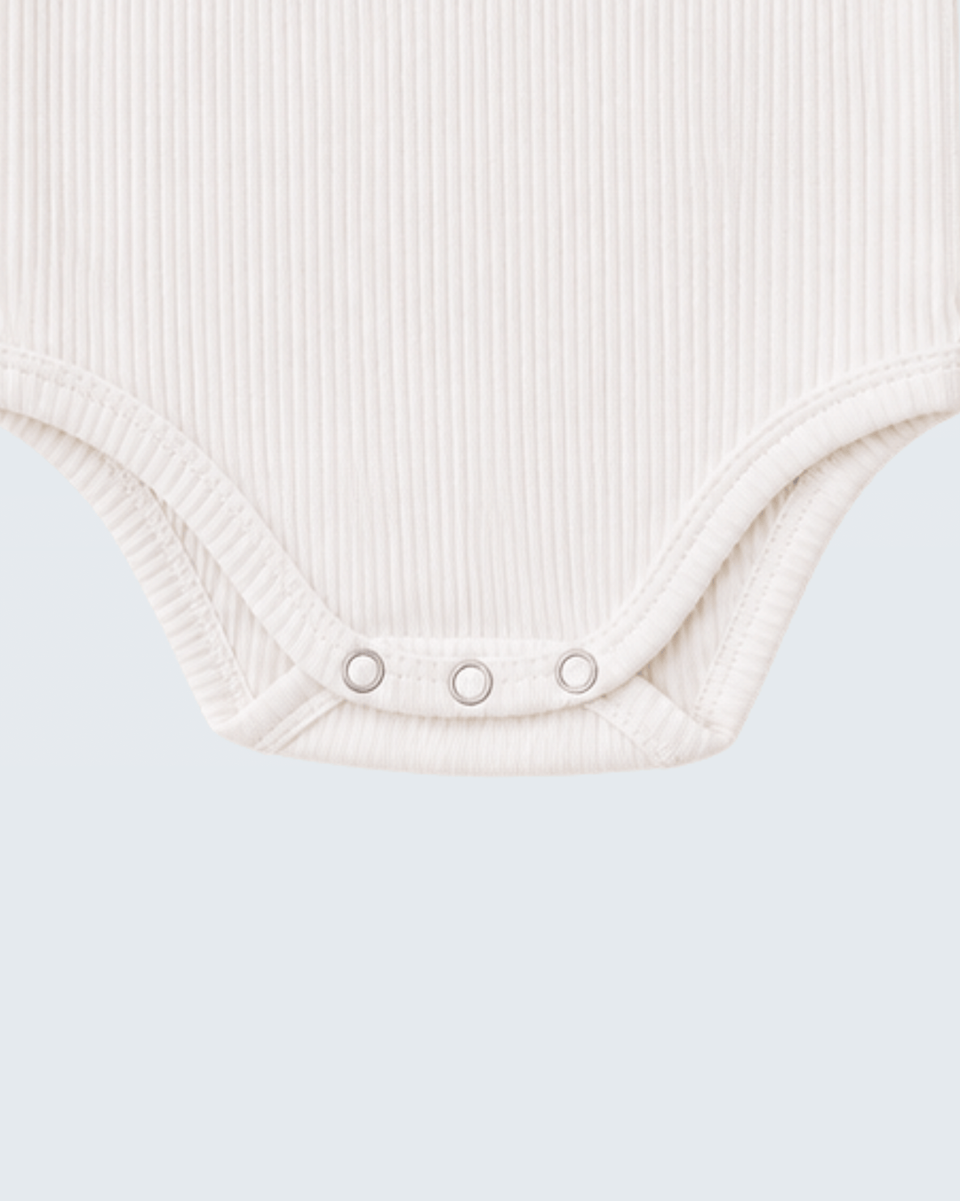 Close-up of a ribbed off-white baby bodysuit showing the crotch area with three silver snap buttons, set against a solid light gray background.