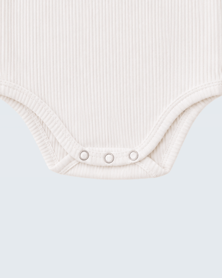 Close-up of a ribbed off-white baby bodysuit showing the crotch area with three silver snap buttons, set against a solid light gray background.
