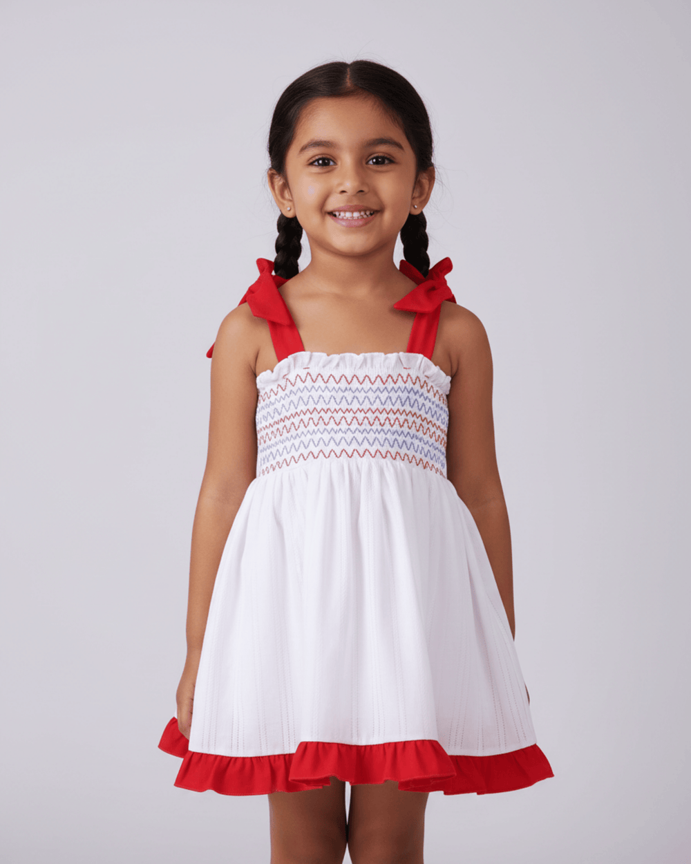 Young girl wearing a white dress with red accents on a plain background