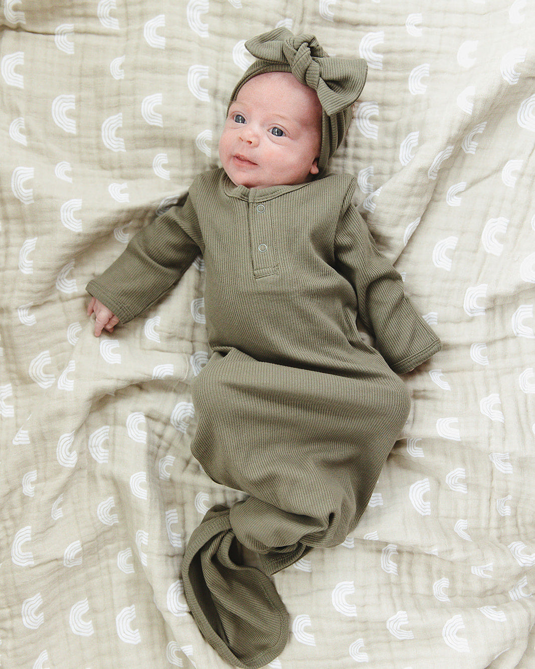 Baby in a green outfit lying on a textured white blanket