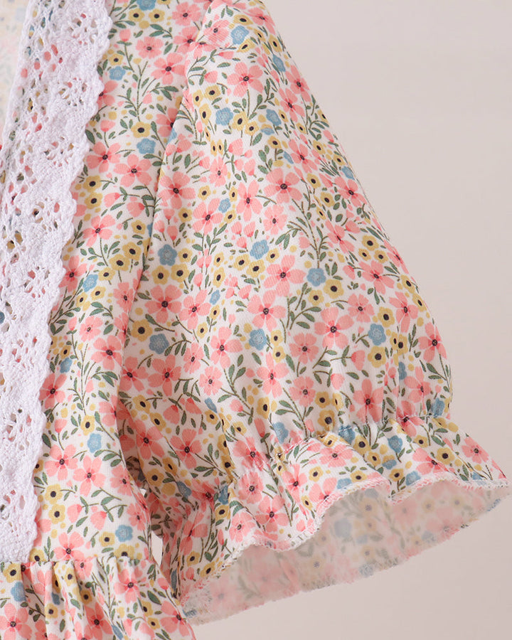 A close-up of a floral-patterned fabric garment, showing a ruffled sleeve with pink, yellow, and blue flowers on a light background, alongside a white lace trim.