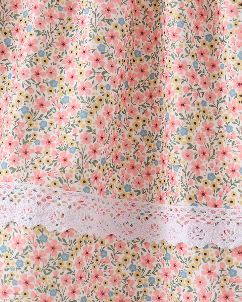 Close-up of a floral fabric with pink, yellow, and blue flowers on a light background, featuring a white lace trim band across the middle.