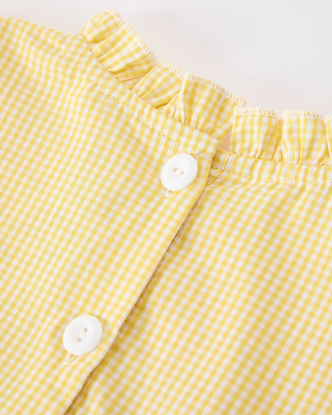 Close-up of a yellow gingham fabric with white buttons on a light gray background