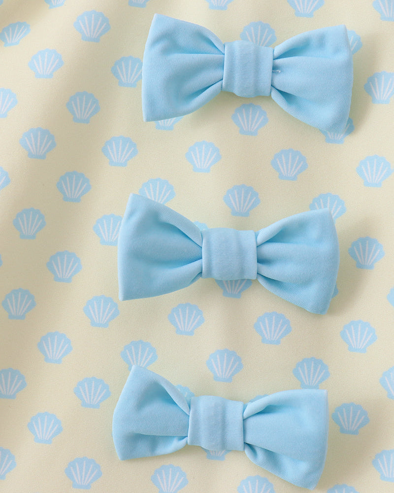 Three light blue bow ties on a beige background with shell pattern