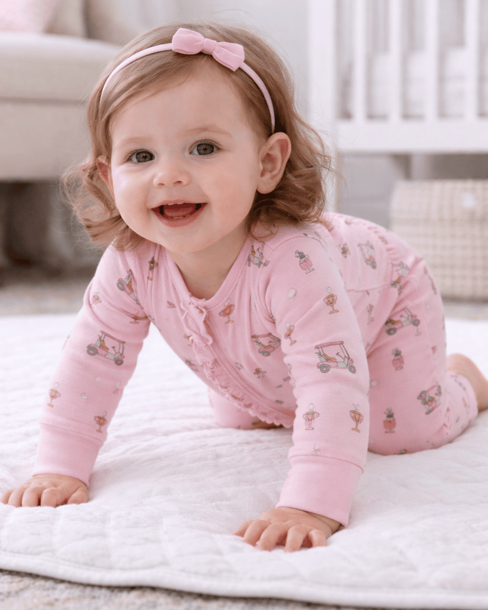 Baby in pink pajamas with a bow sitting on a white blanket