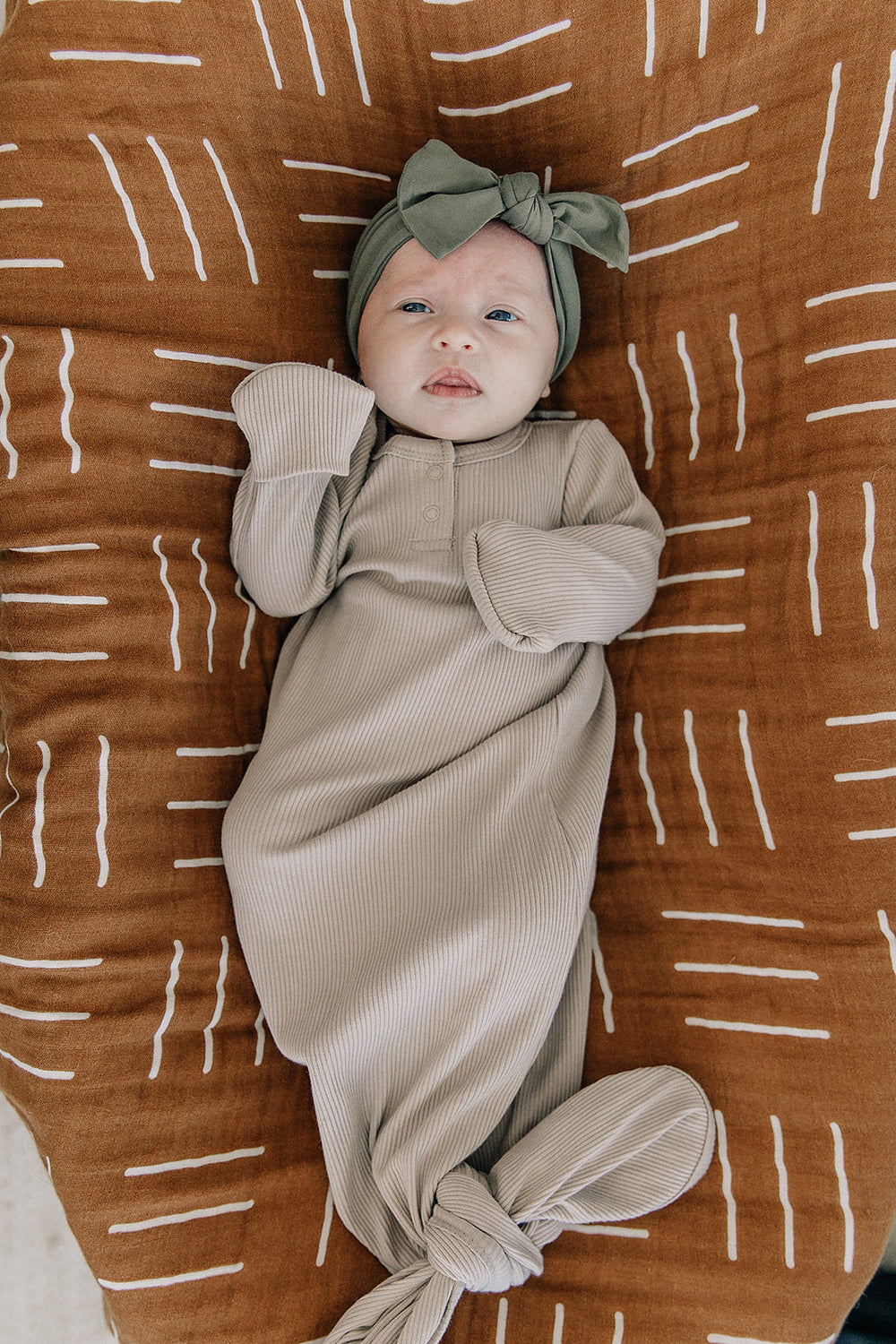 Beige ribbed baby knot gown on infant, long sleeves and snap-button front.